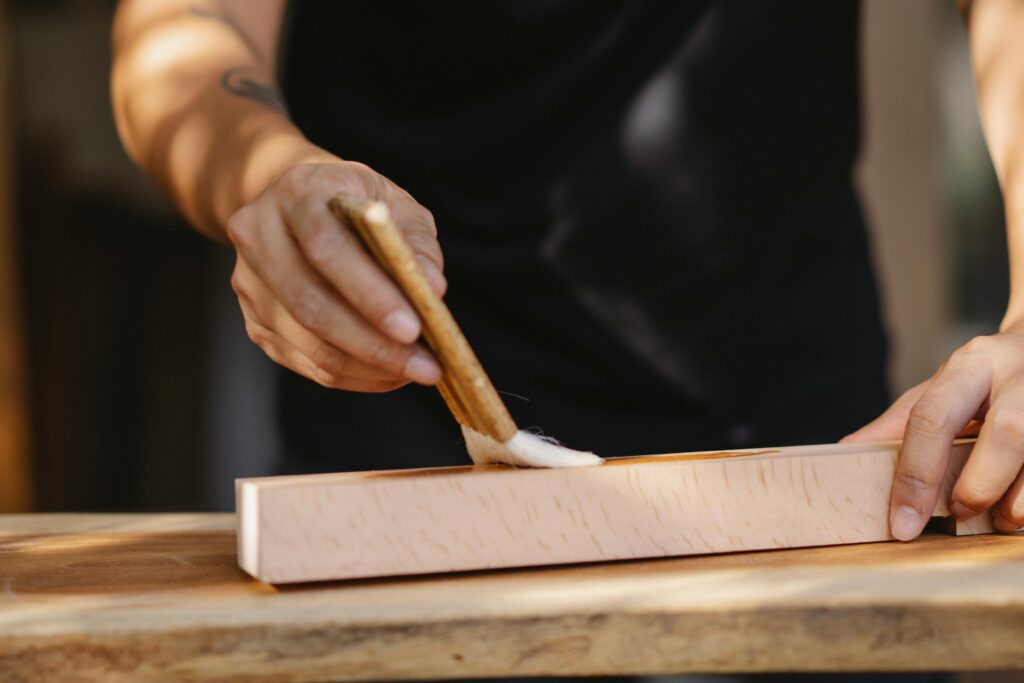 A male craftsman carefully applies varnish to a wooden surface, showcasing artisanal skill.